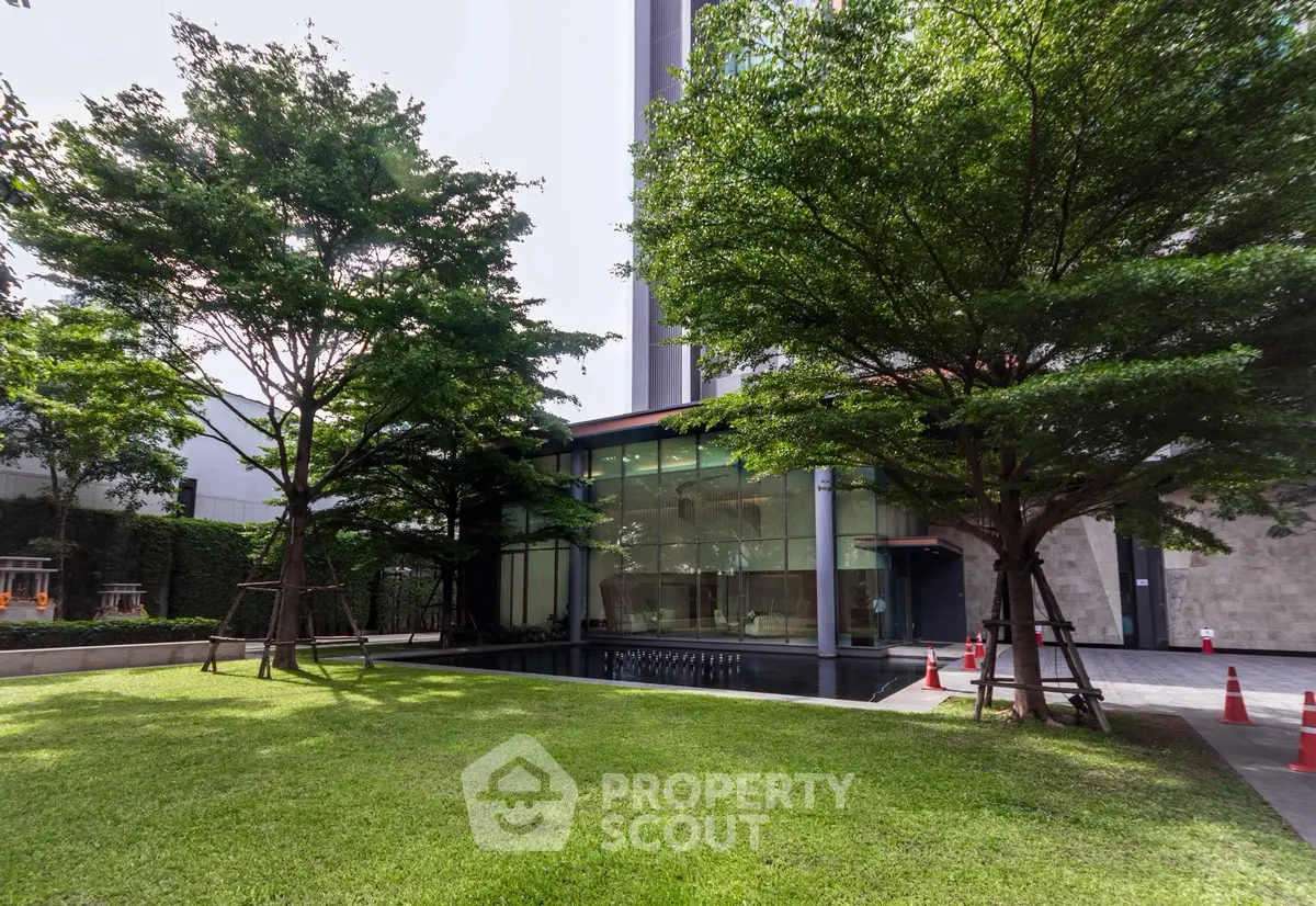 Modern building exterior with lush green garden and glass facade, perfect for urban living.