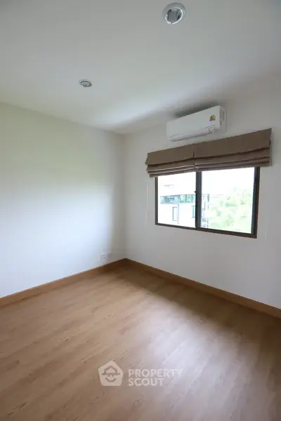 Spacious empty room with wooden flooring and large window, perfect for customization.