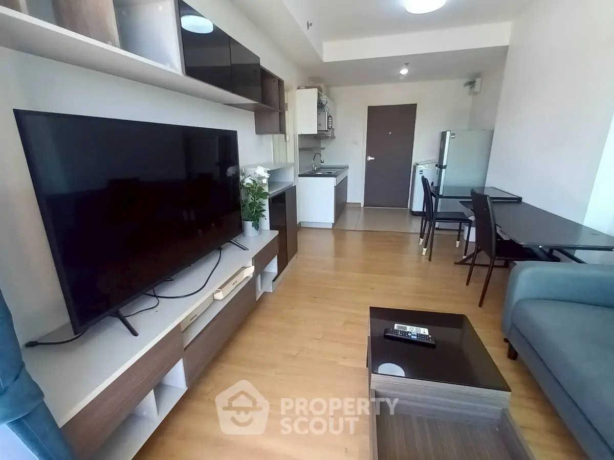 Modern living room with open kitchen layout, featuring sleek furniture and a large TV, perfect for urban living.