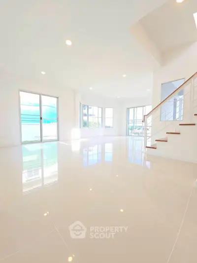 Spacious modern living room with large windows and elegant staircase, perfect for natural light lovers.