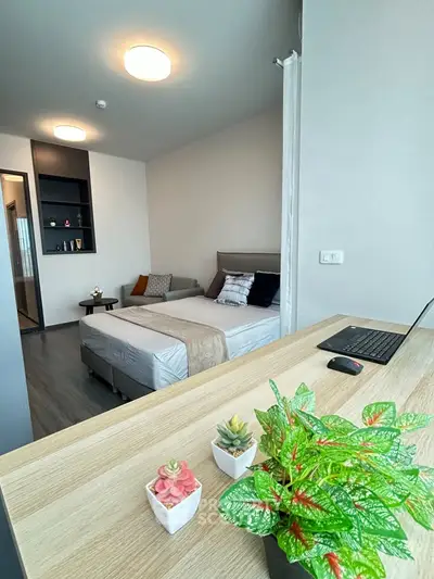 Modern bedroom with stylish decor and workspace, featuring cozy bed and vibrant plants.