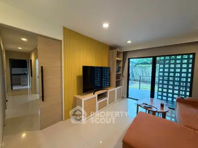 Modern living room with large TV, stylish furniture, and garden view through sliding doors.