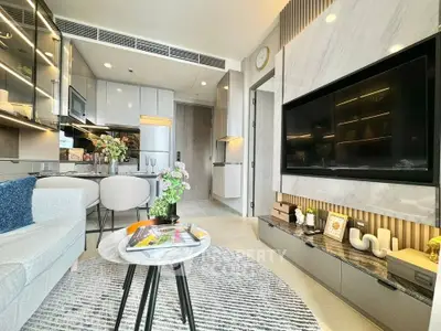 Modern living room with sleek design, featuring a large TV, stylish furniture, and an open kitchen layout.