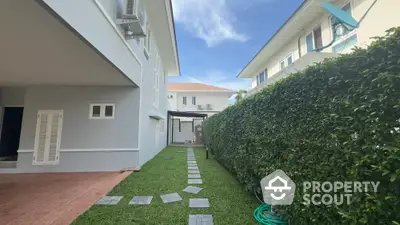 Charming garden pathway between modern homes with lush greenery and clear blue sky.