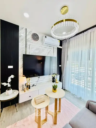 Luxurious modern living room with elegant chandelier and large TV, featuring stylish decor and natural light.