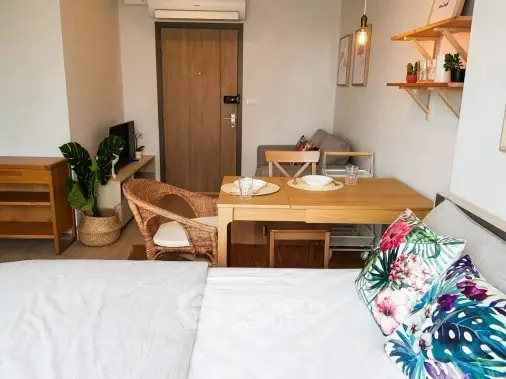 Cozy studio apartment with modern decor and vibrant cushions, featuring a compact dining area and natural light.