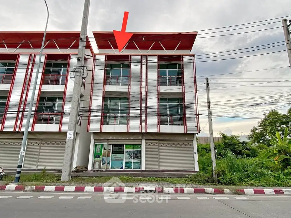 Modern commercial building exterior with red accents and large windows on a busy street.
