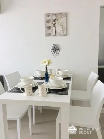 Modern dining area with elegant white table and chairs, set for a cozy meal.