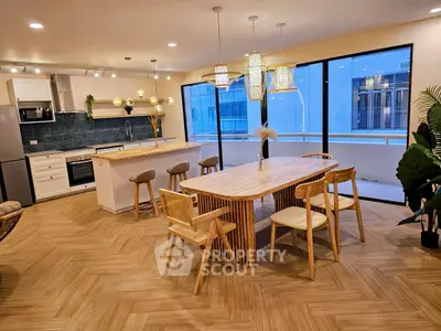 Modern kitchen with open layout and stylish dining area, featuring elegant lighting and large windows.