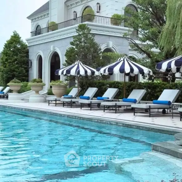 Luxurious poolside area with elegant loungers and striped umbrellas at a grand estate.
