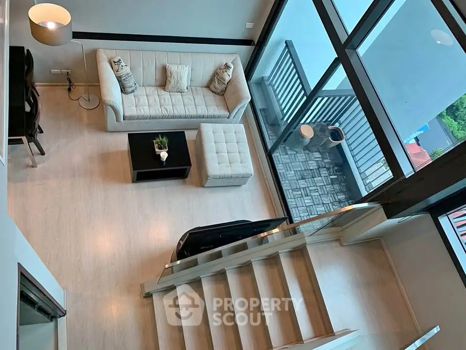 Modern loft-style living room with high ceilings and large windows overlooking a balcony.