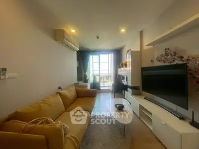 Modern living room with cozy yellow sofa and large TV, bright natural light from balcony.