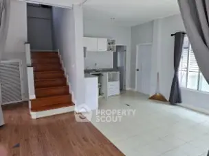 Spacious open-plan living area with modern kitchen and wooden staircase, perfect for family gatherings.