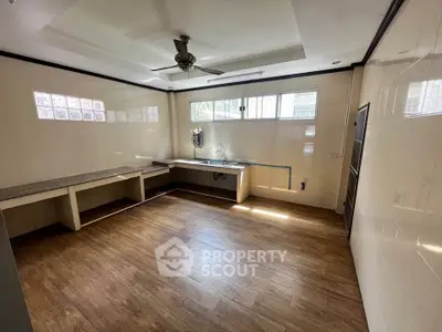 Spacious kitchen with wooden flooring and ample natural light, featuring a ceiling fan and large windows.