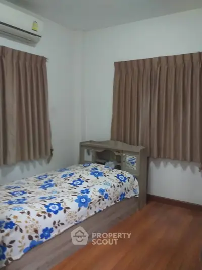 Cozy bedroom with wooden flooring and floral bedding, featuring air conditioning and natural light.