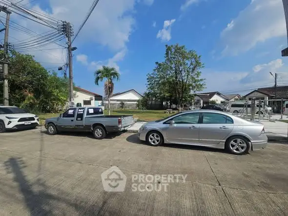 Charming suburban neighborhood with parked cars and lush greenery under a clear blue sky.