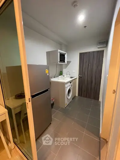 Compact kitchen with modern appliances including fridge, microwave, and washing machine in a cozy apartment.