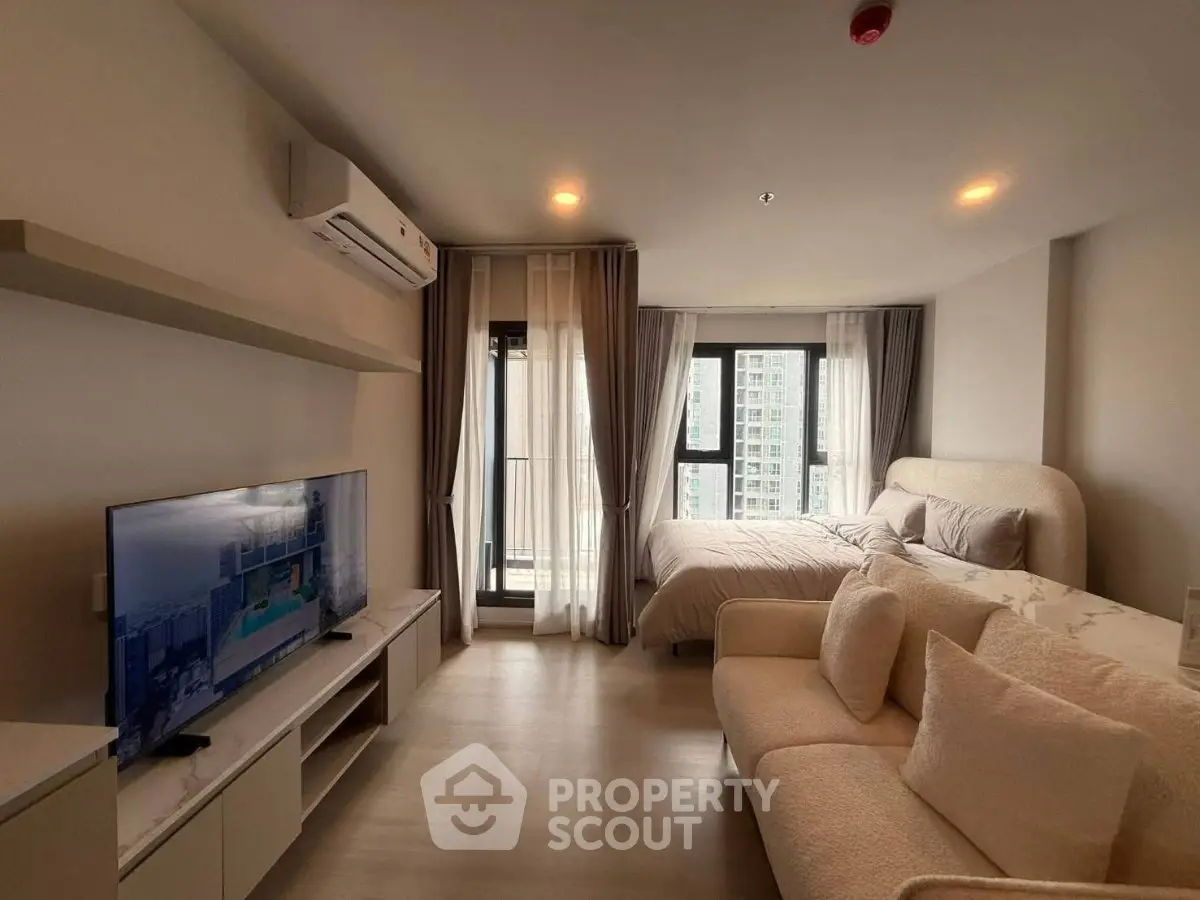 Modern studio apartment with cozy living area and large windows offering city views.