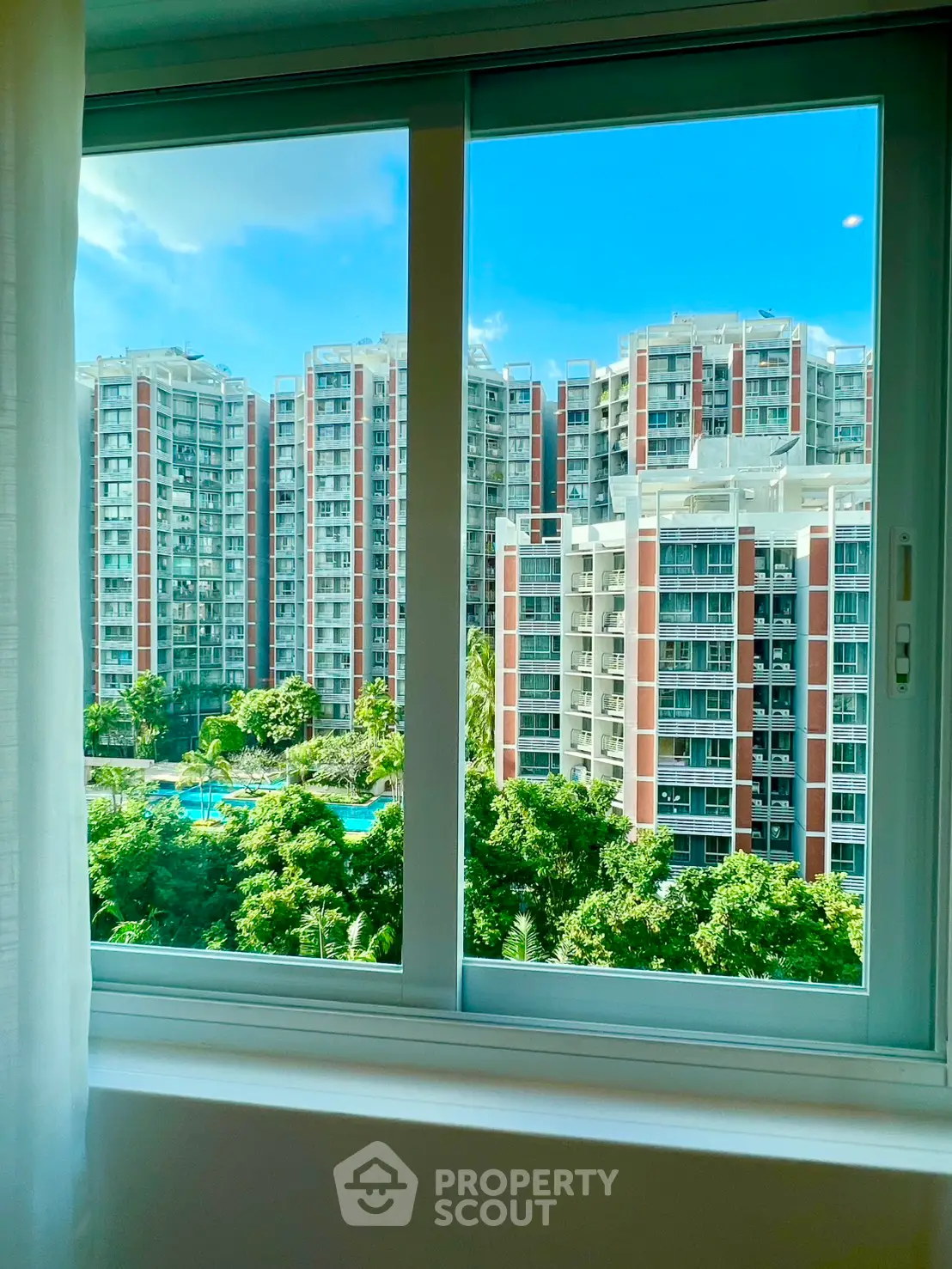 Stunning view of modern high-rise buildings from a window, showcasing lush greenery and a pool.