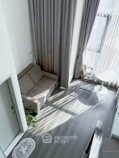 Modern living room with high ceilings and large windows, featuring a cozy sofa and elegant curtains.