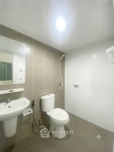 Modern bathroom with sleek fixtures and neutral tiles, featuring a shower and toilet.