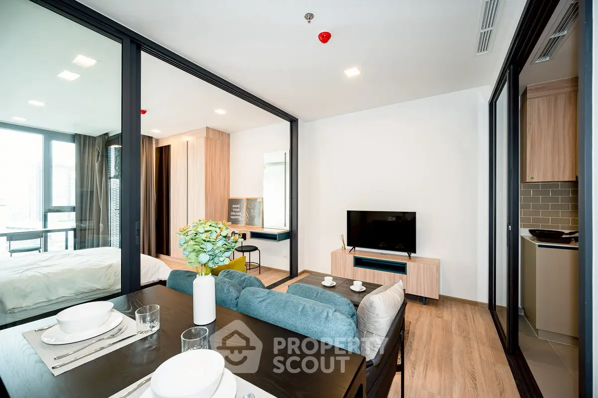 Modern open-plan living room with dining area and bedroom, featuring sleek glass partitions and contemporary decor.