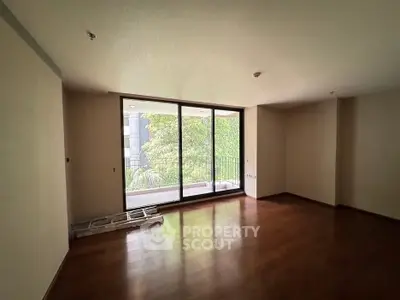 Spacious empty room with large window and wooden flooring