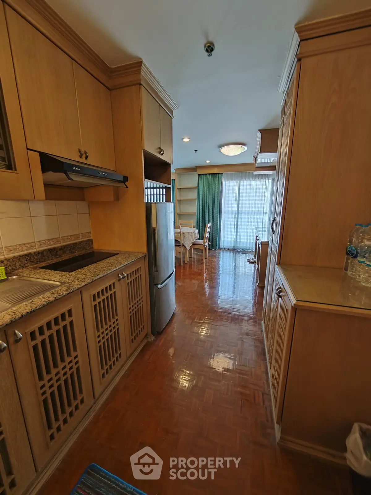 Charming kitchen with wooden cabinetry and open layout leading to a bright dining area with large windows.