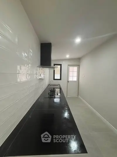 Sleek modern kitchen with black countertop and gas stove, featuring minimalist design and ample natural light.