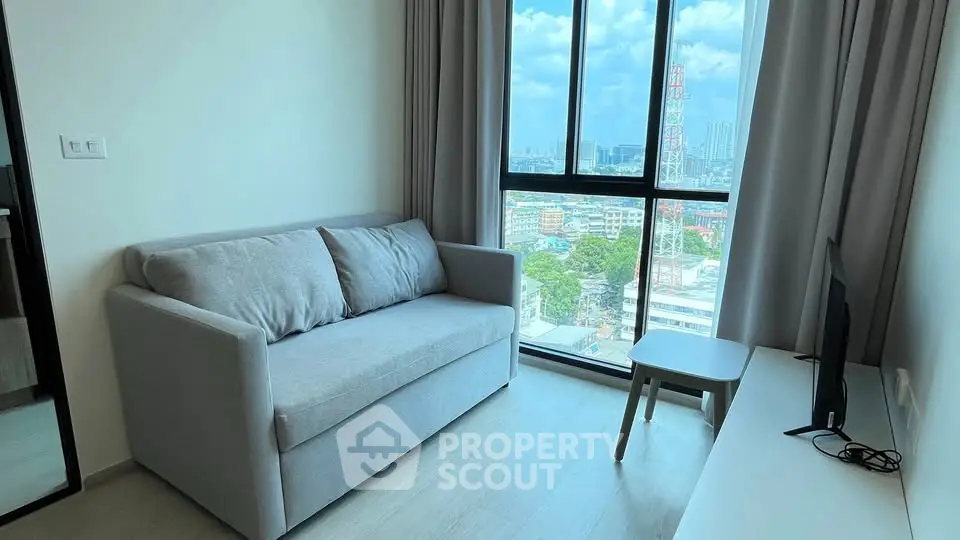 Modern living room with city view, featuring a cozy gray sofa and large window.