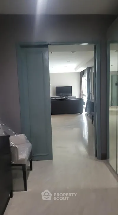Modern apartment hallway leading to a spacious living room with sleek furniture and a large TV.