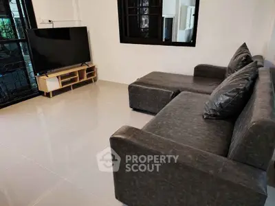 Modern living room with sleek black leather sofa and flat-screen TV, perfect for relaxation and entertainment.