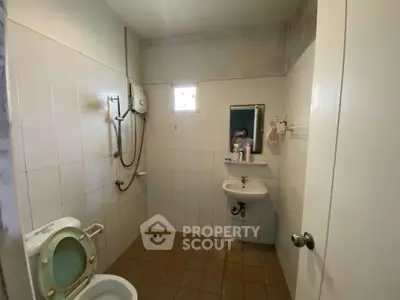 Modest bathroom with shower, toilet, and sink in a tiled setting.