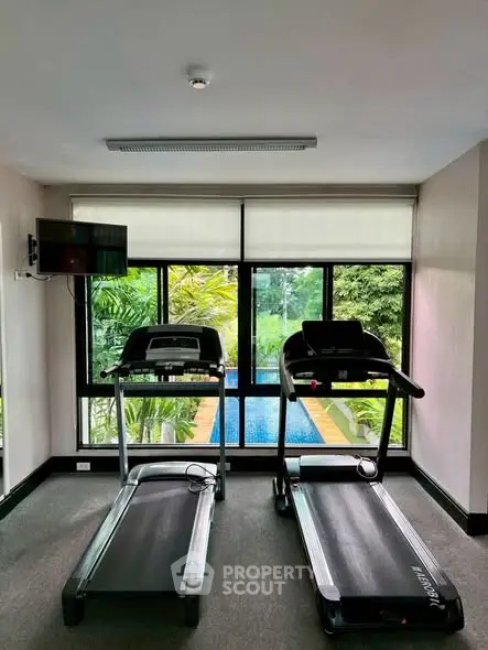 Modern gym with treadmills overlooking lush greenery and pool view, perfect for fitness enthusiasts.