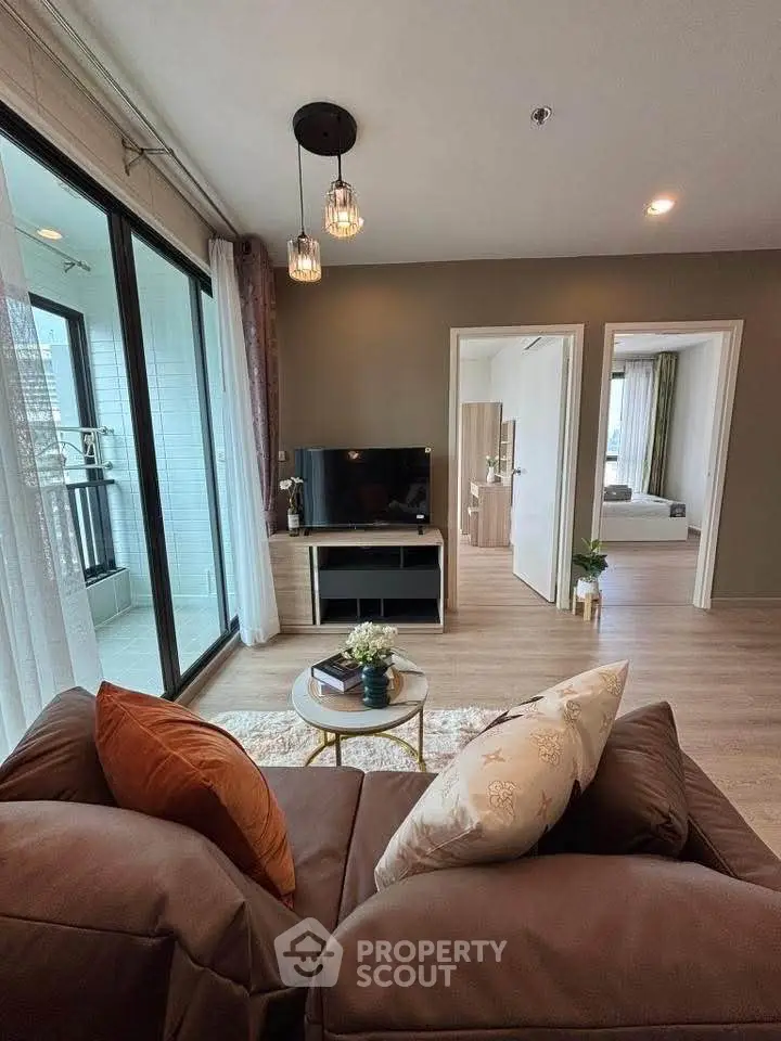 Modern living room with cozy sofa and TV, leading to a bright balcony and bedroom.