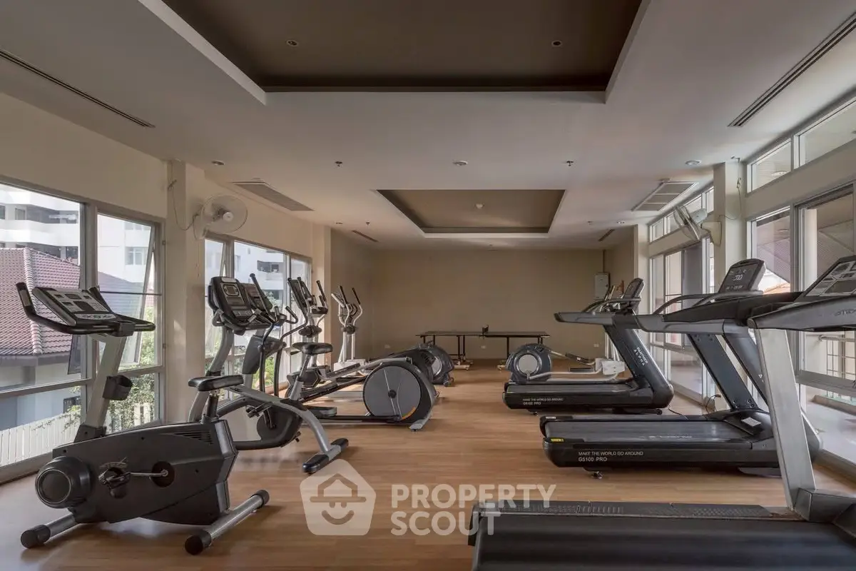 Spacious gym with modern fitness equipment and large windows offering natural light.