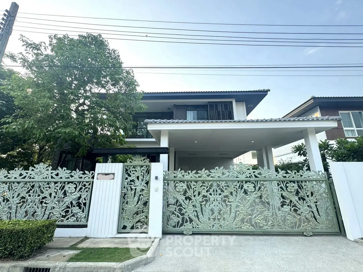 Elegant two-story house with decorative gate and lush greenery, perfect for family living.