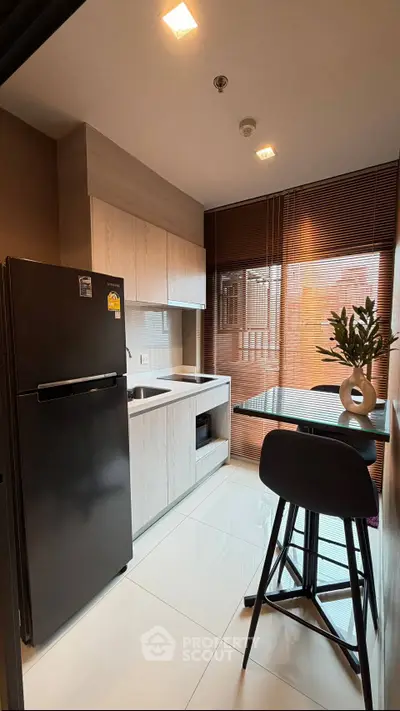 Modern kitchen with sleek black fridge and stylish dining area in a contemporary apartment.