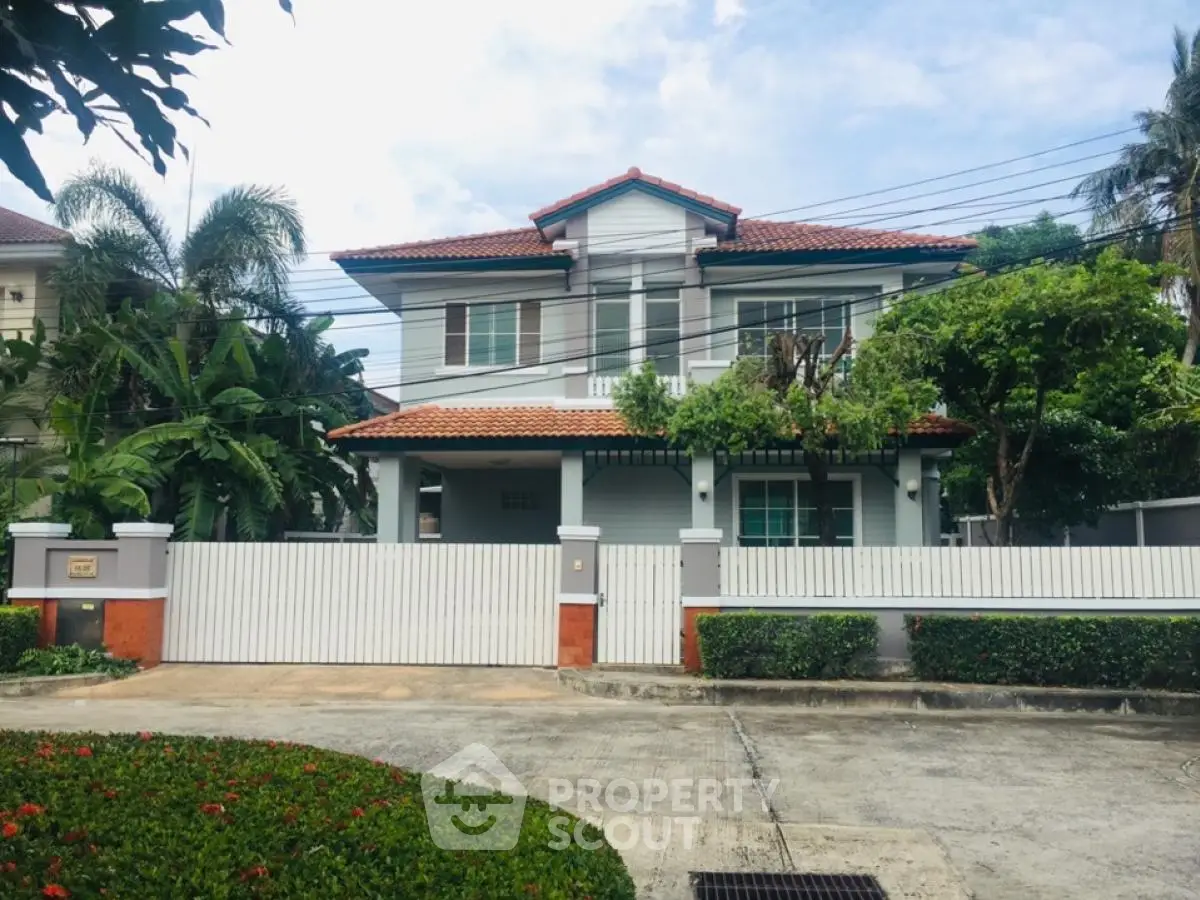 Charming two-story house with red-tiled roof and lush greenery in a serene neighborhood.