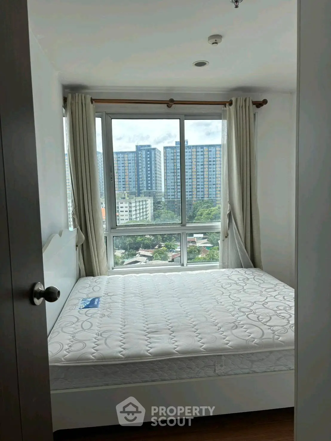 Cozy bedroom with large window offering stunning city views in modern apartment.