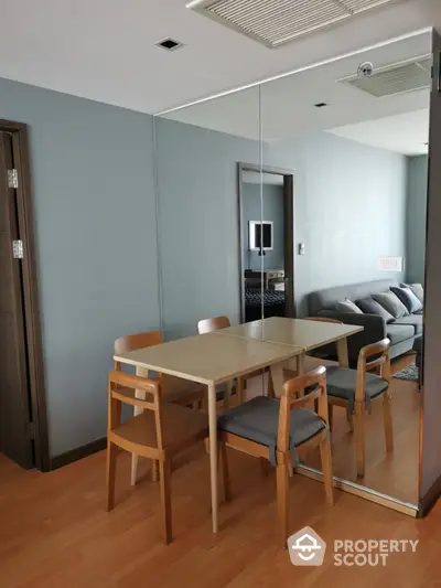 Modern dining area with wooden table and chairs, mirrored wall, and cozy living room view.