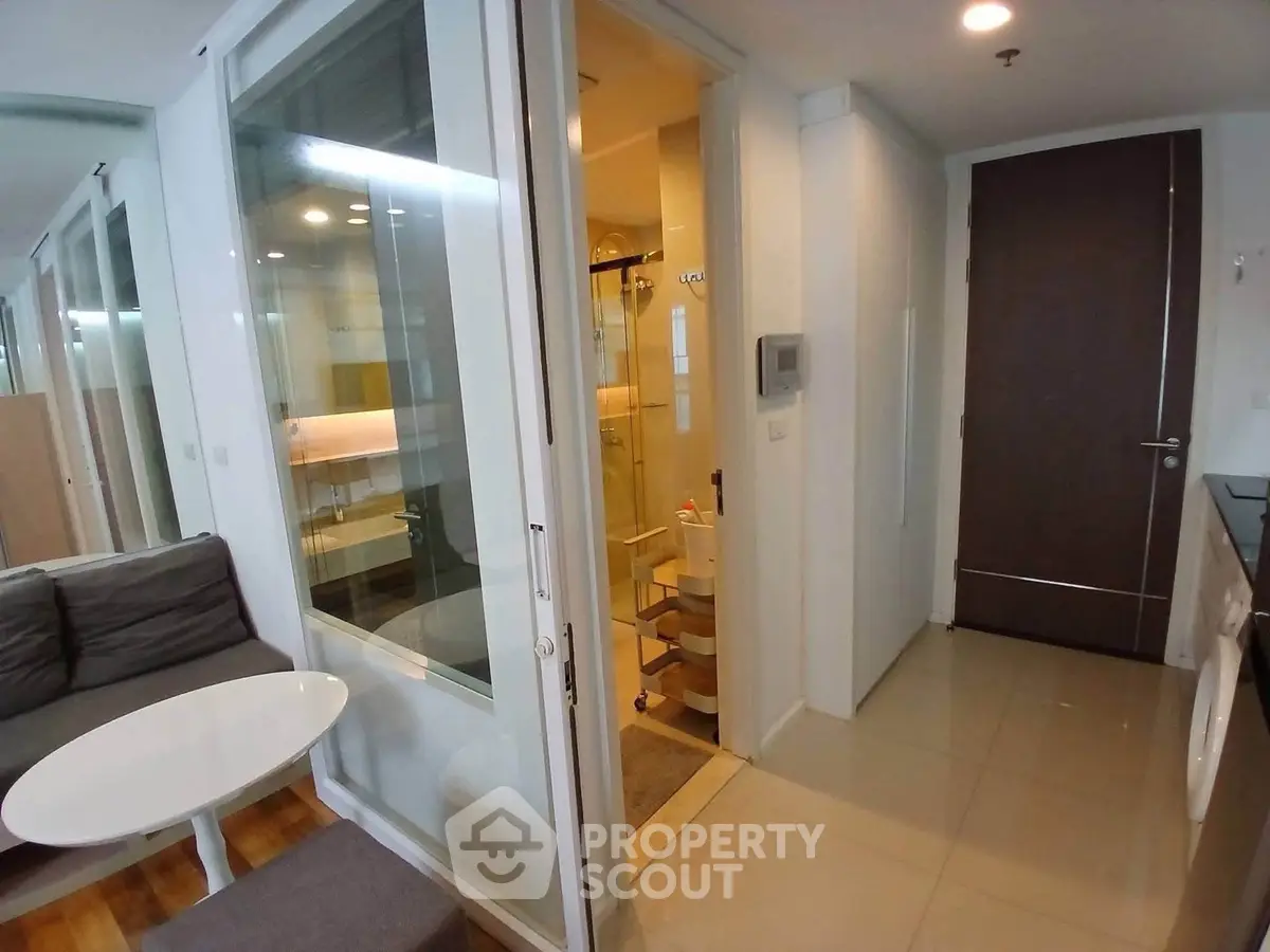Modern apartment interior with glass partition, cozy living area, and sleek bathroom design.