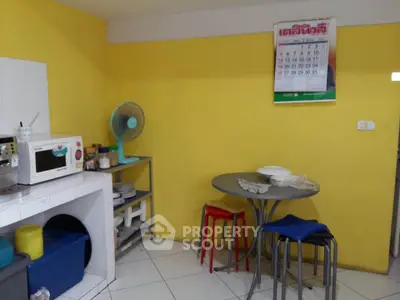 Cozy kitchen with vibrant yellow walls, featuring a microwave, fan, and small dining area.