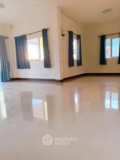 Spacious sunlit living room with glossy tiled floors and large windows with blue curtains.