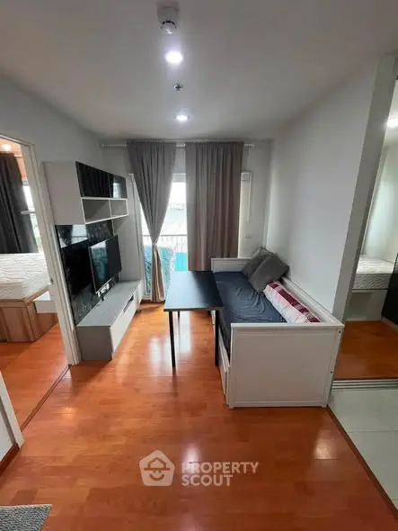Modern living room with sleek furniture and wooden flooring, featuring a cozy sofa and wall-mounted TV.