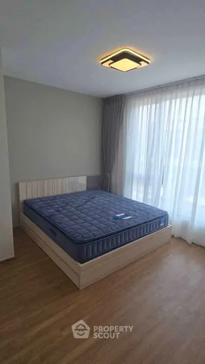 Spacious bedroom with large window and modern lighting in a cozy apartment.