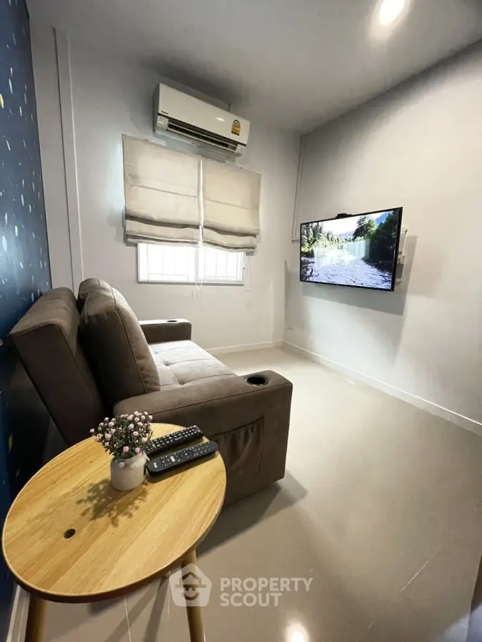 Cozy living room with modern sofa, wall-mounted TV, and air conditioning unit.