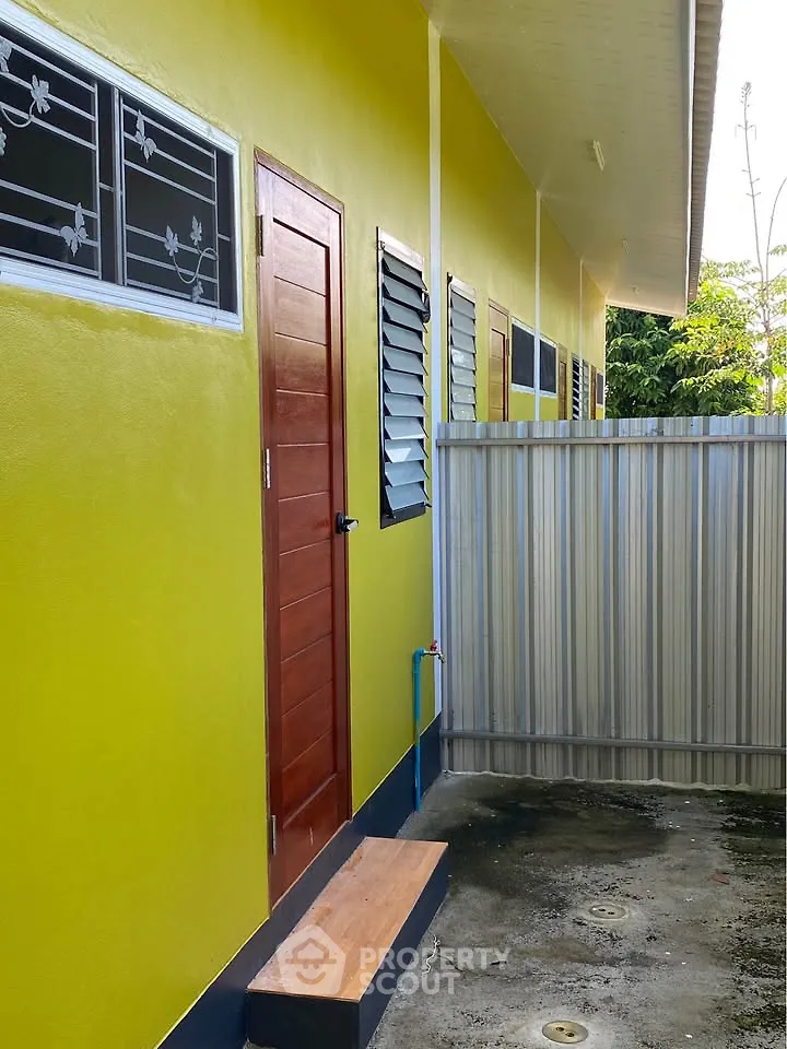 Vibrant yellow exterior of a modern building with wooden door and metal fence.
