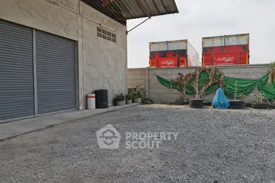 Industrial warehouse exterior with gravel yard and storage containers.