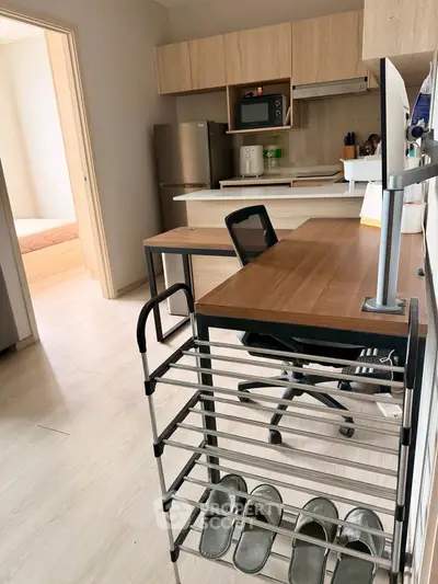 Modern studio apartment with compact kitchen and workspace, featuring sleek wooden cabinetry and light flooring.